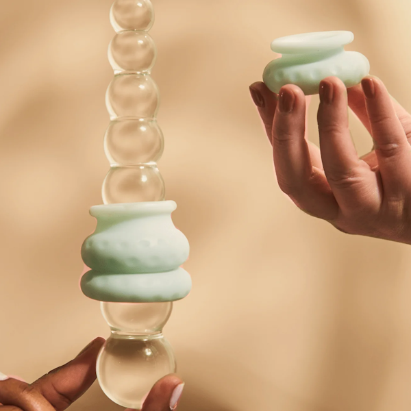 Hands holding a textured glass pleasure wand with mint silicone sleeve on beige background