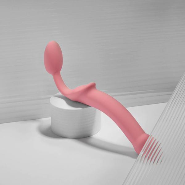 Pink silicone curved dual-ended adult toy on white cylindrical stand, modern minimal background.