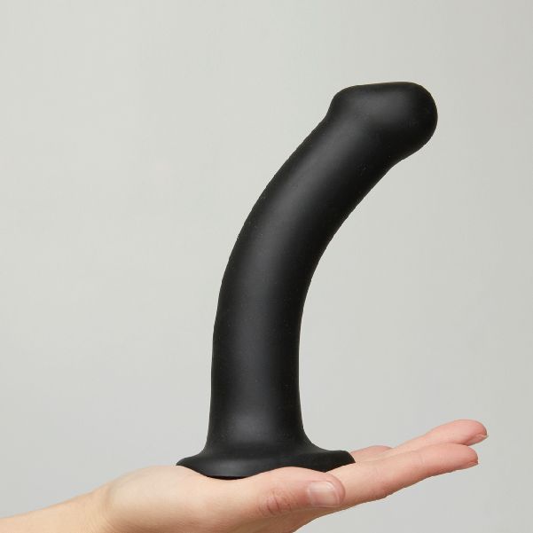 Black silicone dual density dildo with curved shaft, held in hand, against neutral background
