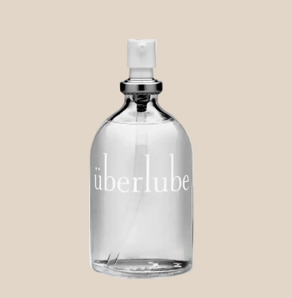 Clear glass bottle of Überlube personal lubricant with pump dispenser on beige background