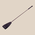 Black faux leather riding crop with textured handle on beige background