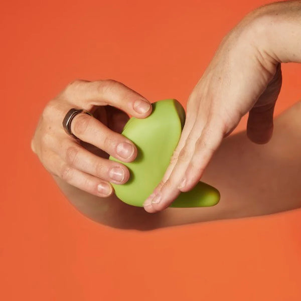 Hand holding a green silicone massage toy against an orange background