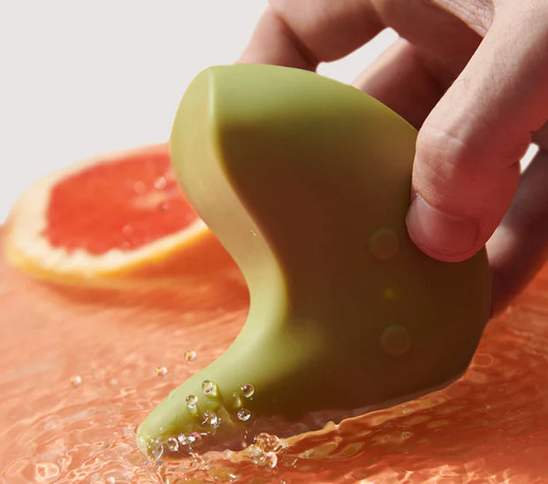 Hand holding waterproof green silicone personal massager in water with grapefruit slice