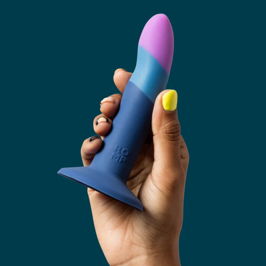 Hand holding a silicone gradient blue and purple adult toy with flared base on teal background.