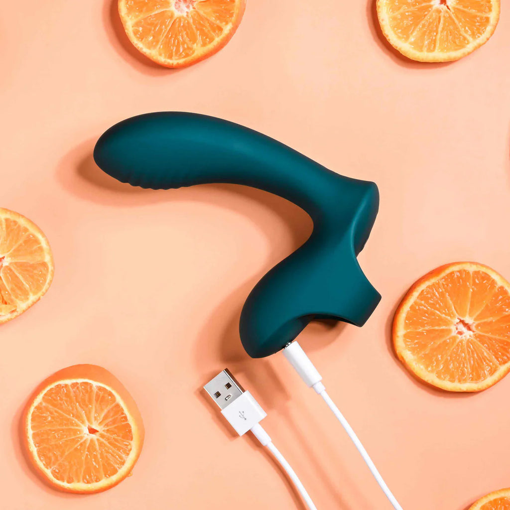 Rechargeable silicone adult toy with USB cable and orange slices on peach background