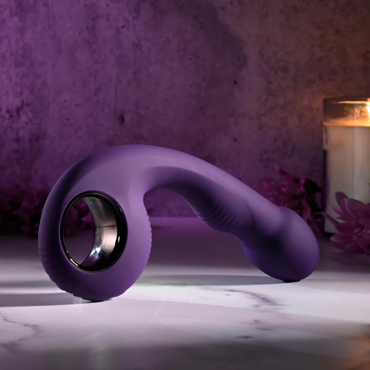 Purple silicone curved adult toy with ergonomic handle on marble surface, soft candlelight