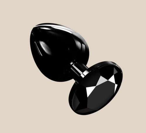 Black jeweled metal butt plug with faceted gemstone base on beige background