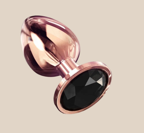 Rose gold metal plug with black gemstone base on beige background