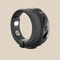 Black silicone vibrating ring with buttons and metallic accents on a beige background