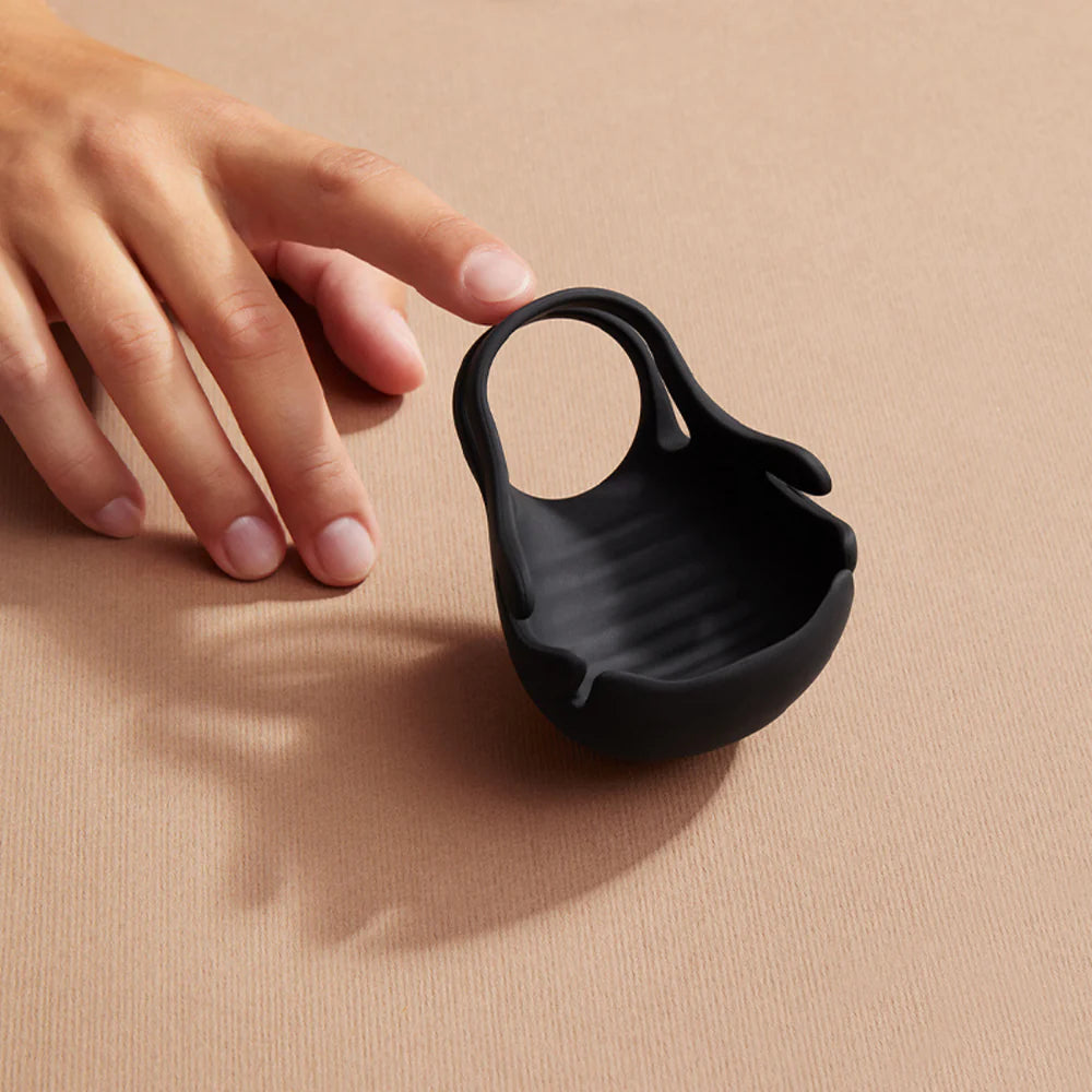 Hand reaching for a black silicone couples toy on a neutral surface