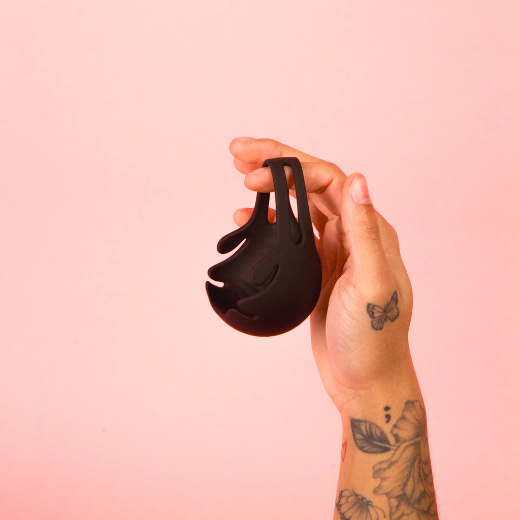 Hand holding a black silicone adult toy with unique open design against a pink background