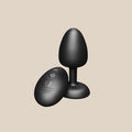Black silicone vibrating plug with remote control on beige background, adult toy
