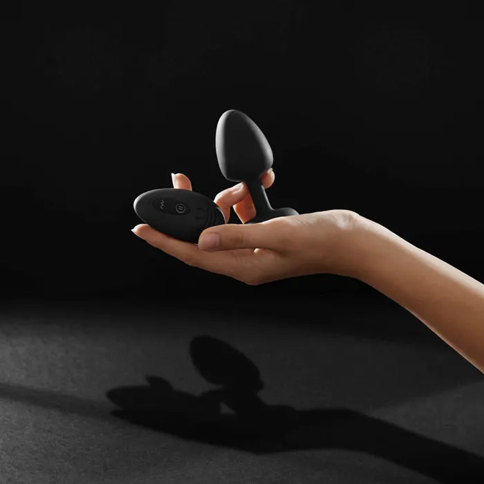 Hand holding a black silicone remote control plug against a dark background.