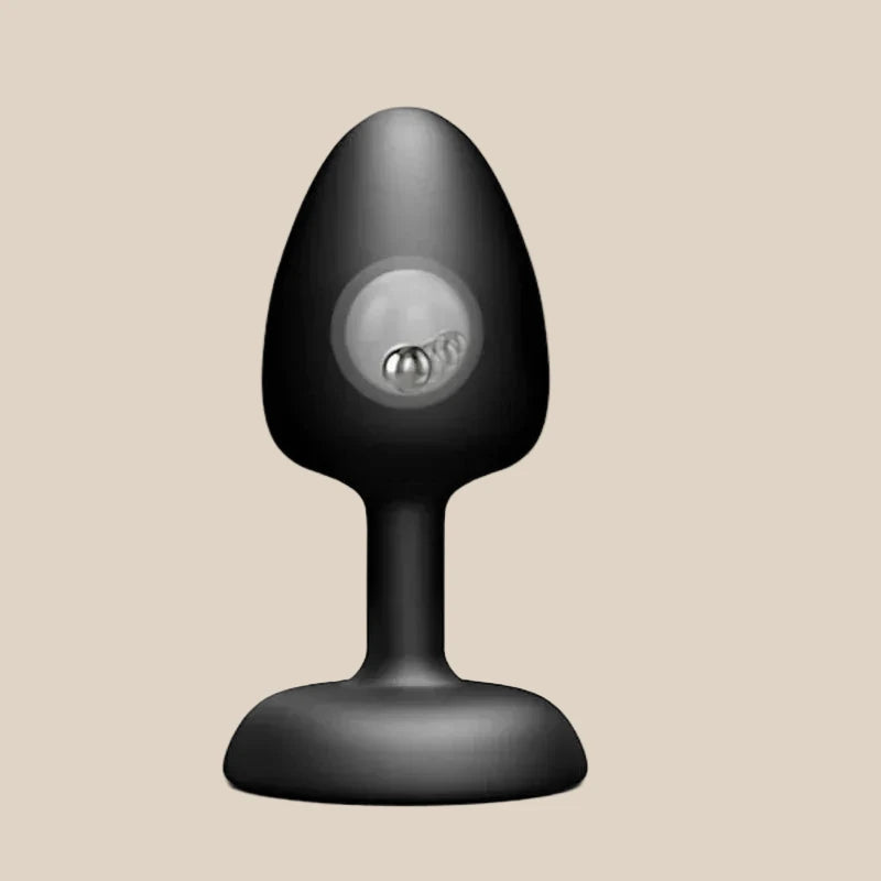 Black silicone butt plug with a rounded base and internal rolling ball, on beige background