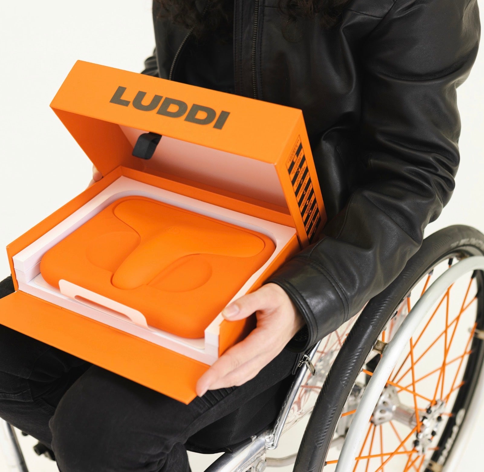 Person in wheelchair holding orange box labeled LUDDI with body-safe silicone product inside