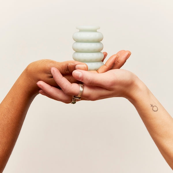 Two hands holding a jade-colored intimacy ring stack against a neutral background.