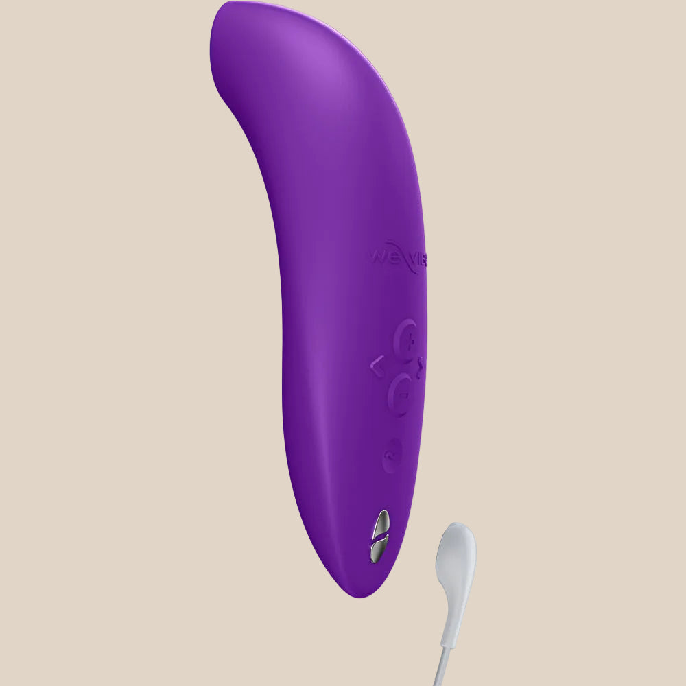 Purple silicone air pulse stimulator with curved design and charging cable on white background