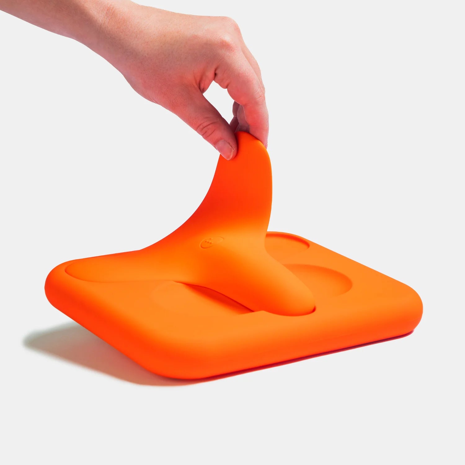 Hand lifting flexible orange wireless magnetic charging station on white background