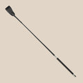 Black faux leather riding crop with slim handle on beige background