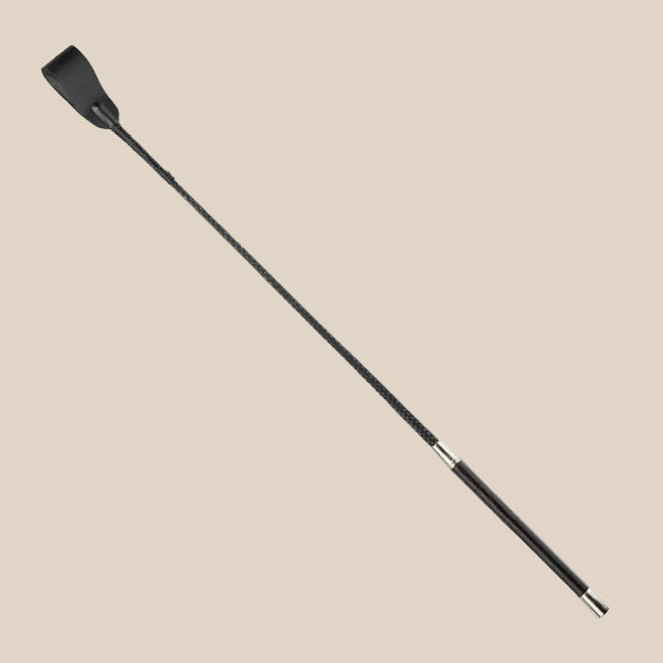 Black faux leather riding crop with slim handle on beige background