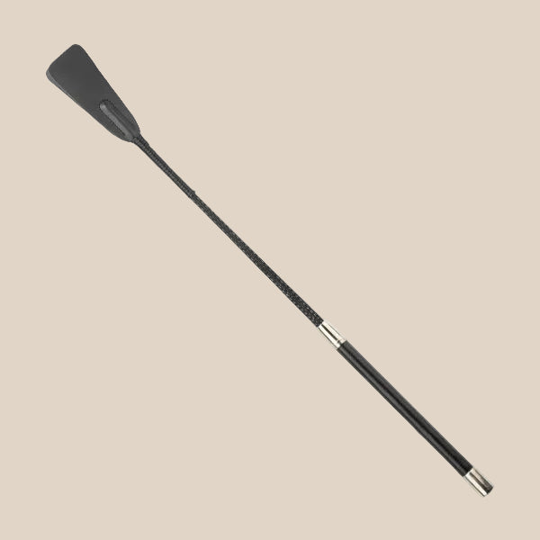 Black faux leather riding crop with a silver-accented handle on a beige background